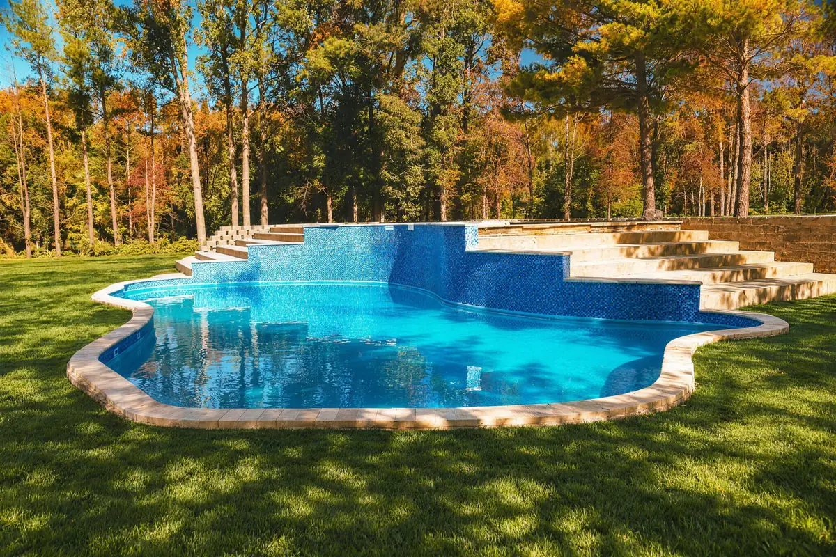 Freeform inground pool with raised blue glass tile wall in Morganville NJ, photographed by The Hype Hero