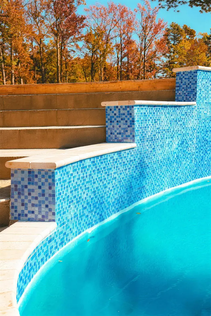 Tiled stair-step pool wall with stone caps and fall trees in Morganville NJ